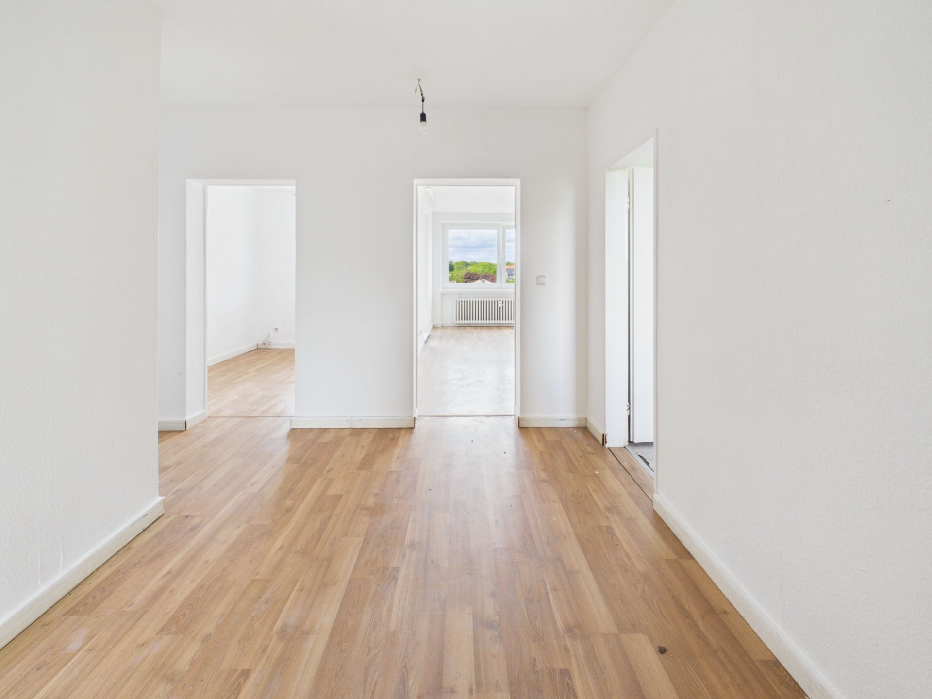 Heller Raum mit Holzboden, weißen Wänden und mehreren offenen Türen zu weiteren Zimmern.