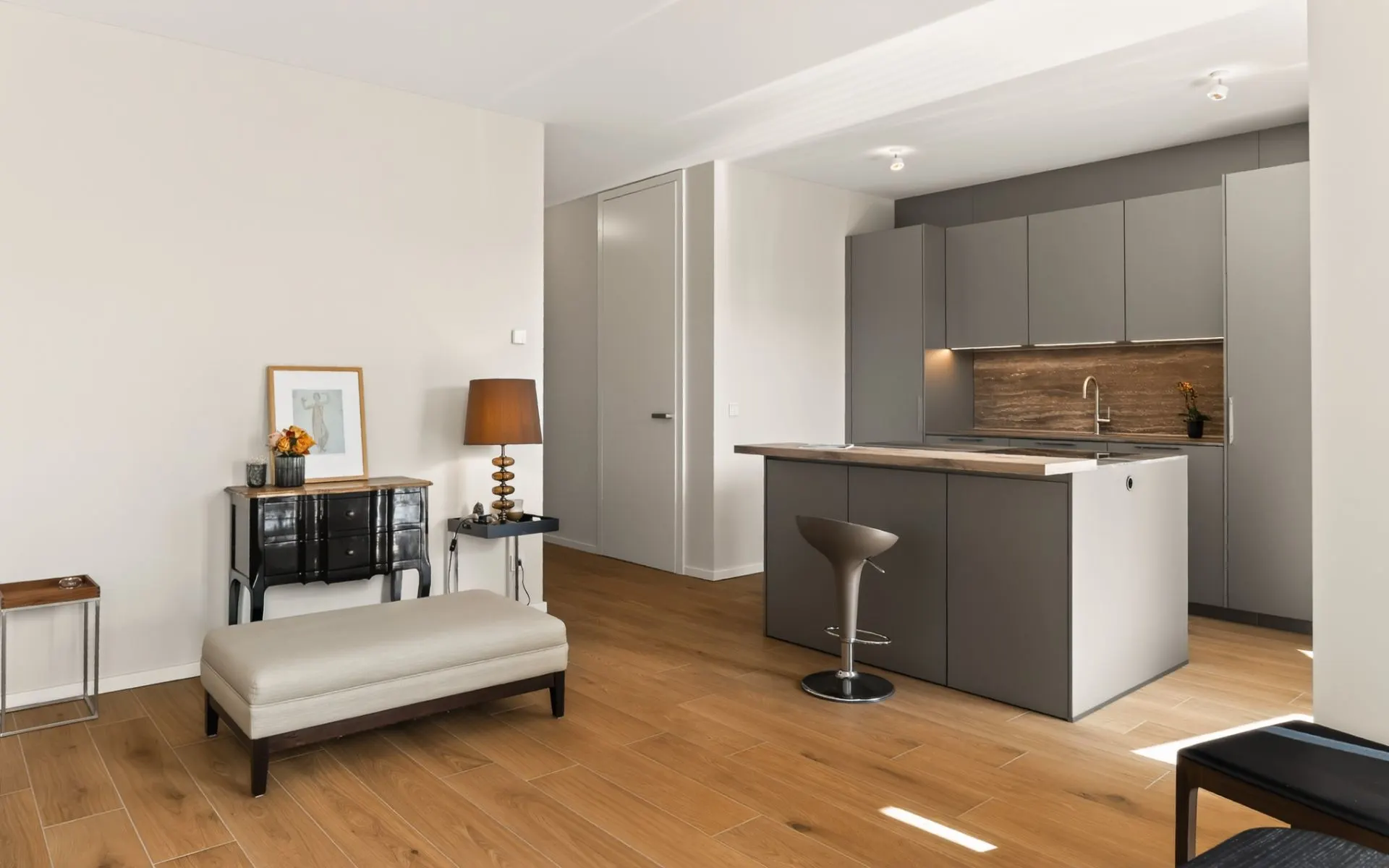 Modernes Wohnzimmer mit offener grauer Küche, Holzboden und heller Wand.