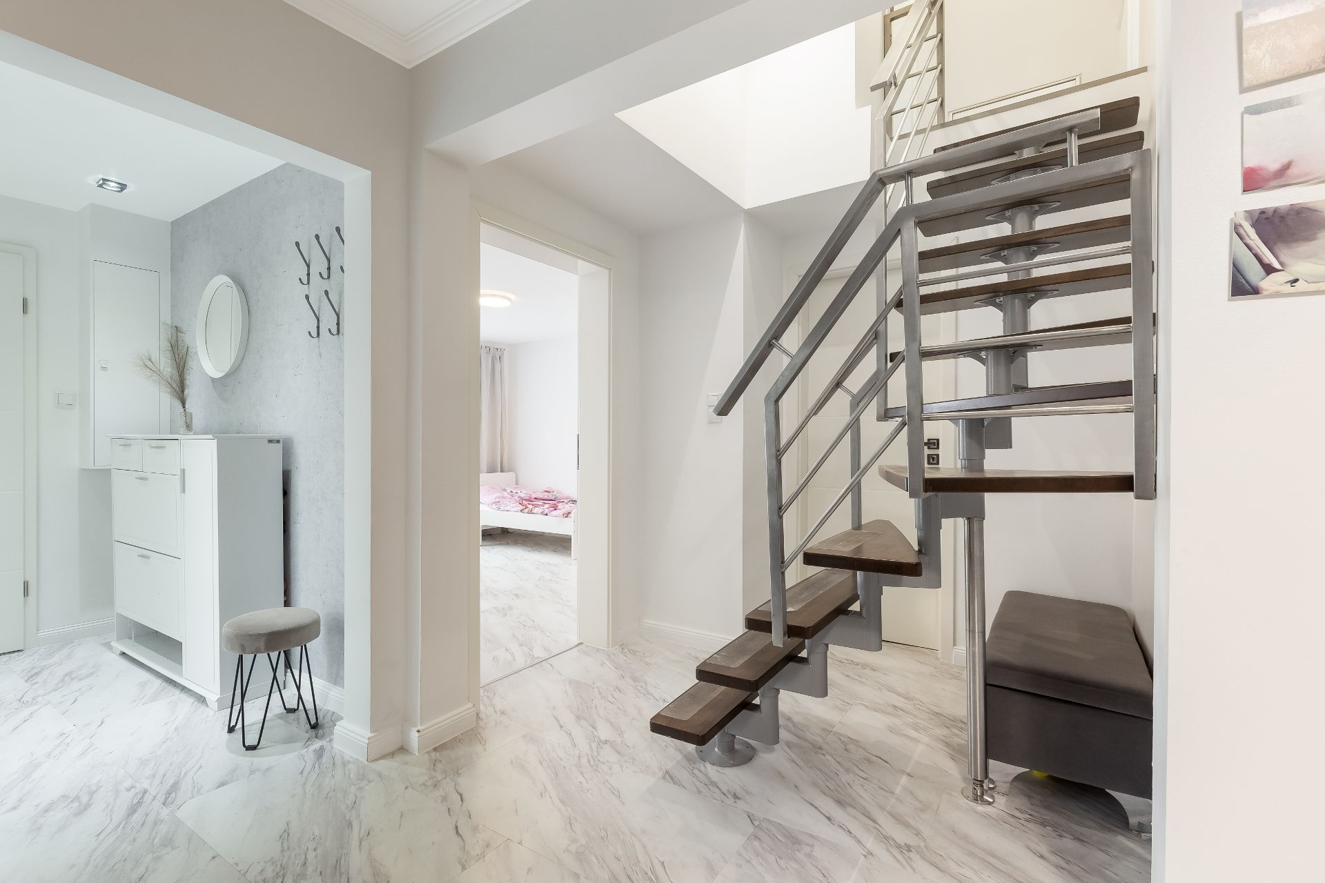 Heller Flur mit moderner Treppe, Kommode, Hocker und Blick ins Schlafzimmer.
