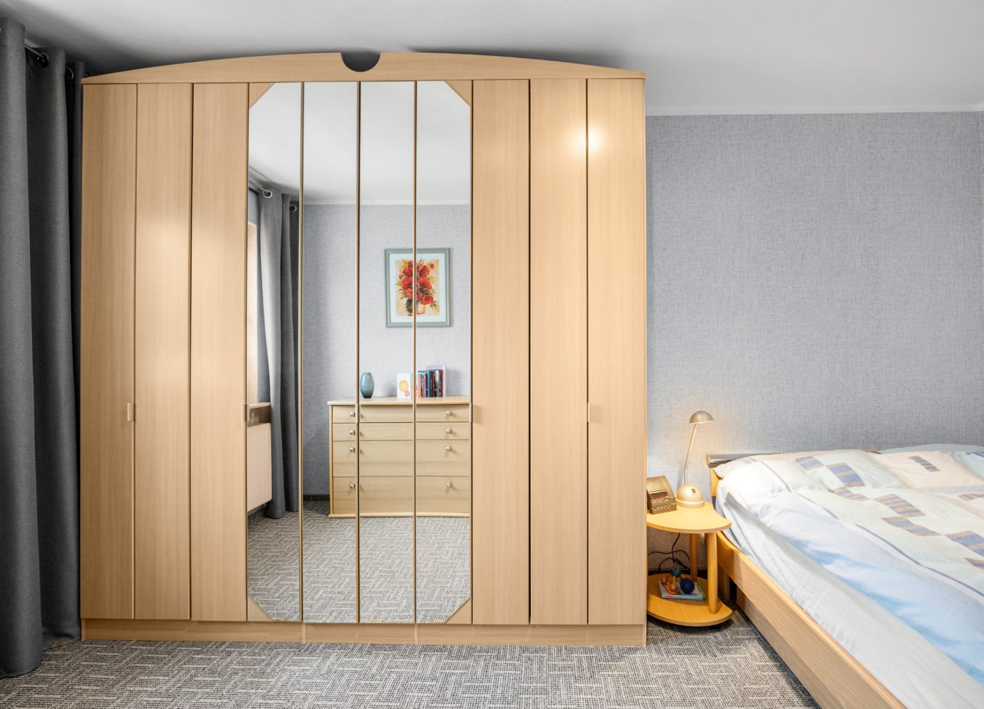 Helles Schlafzimmer mit großem Spiegelschrank, Nachttisch und Bett.