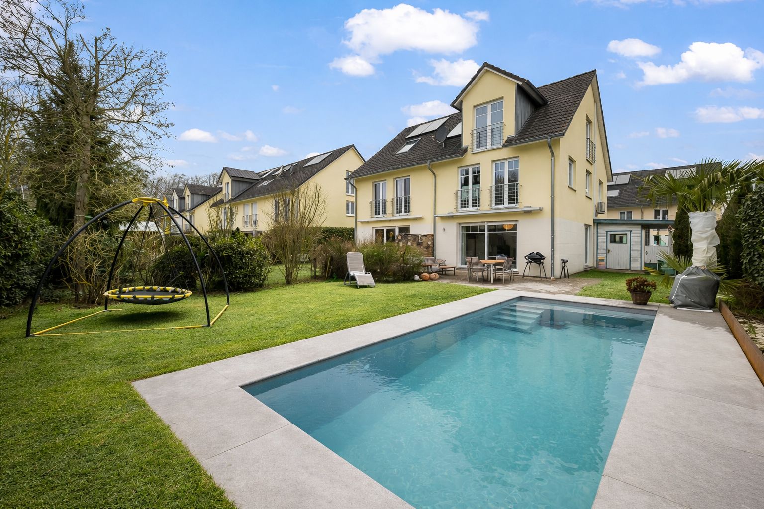 Garten mit großem Pool, Schaukel und Liege vor einem modernen Wohnhaus.