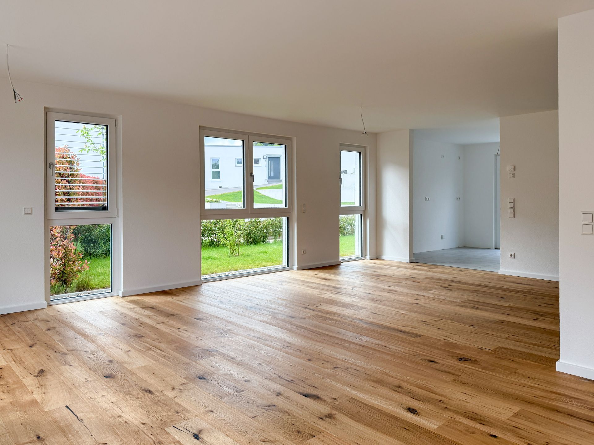 Helles Wohnzimmer mit Holzboden und großen Fenstern, Blick auf Garten.