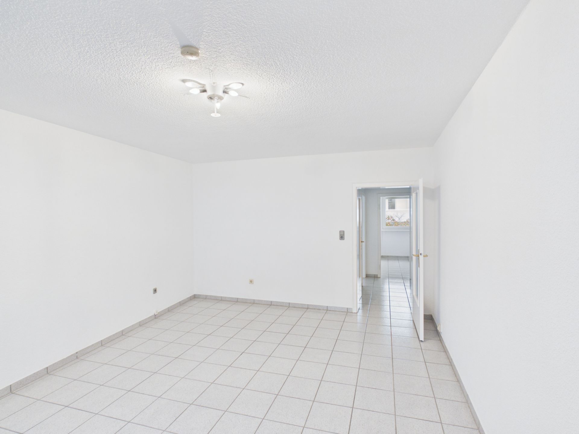 Heller, leerer Raum mit weißen Wänden, Fliesenboden und Deckenleuchte.