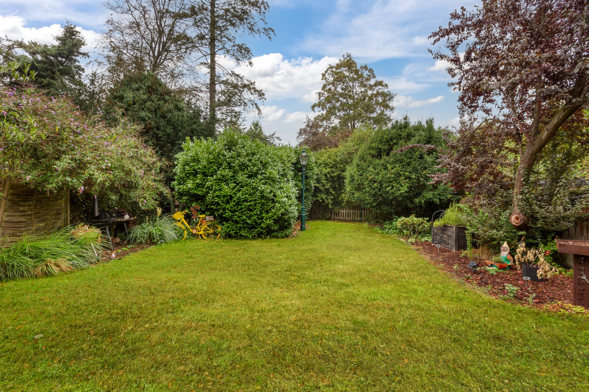 Grüner Garten mit Rasenfläche, Bäumen, Sträuchern und kleinen Gartendekorationen.