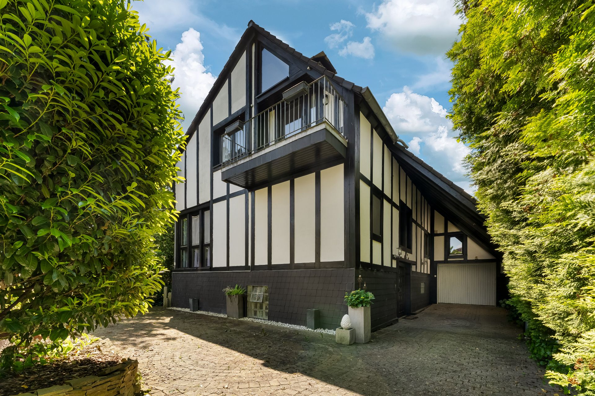 Ein Fachwerkhaus mit Balkon, Garage und umgebenden grünen Büschen bei Tageslicht.