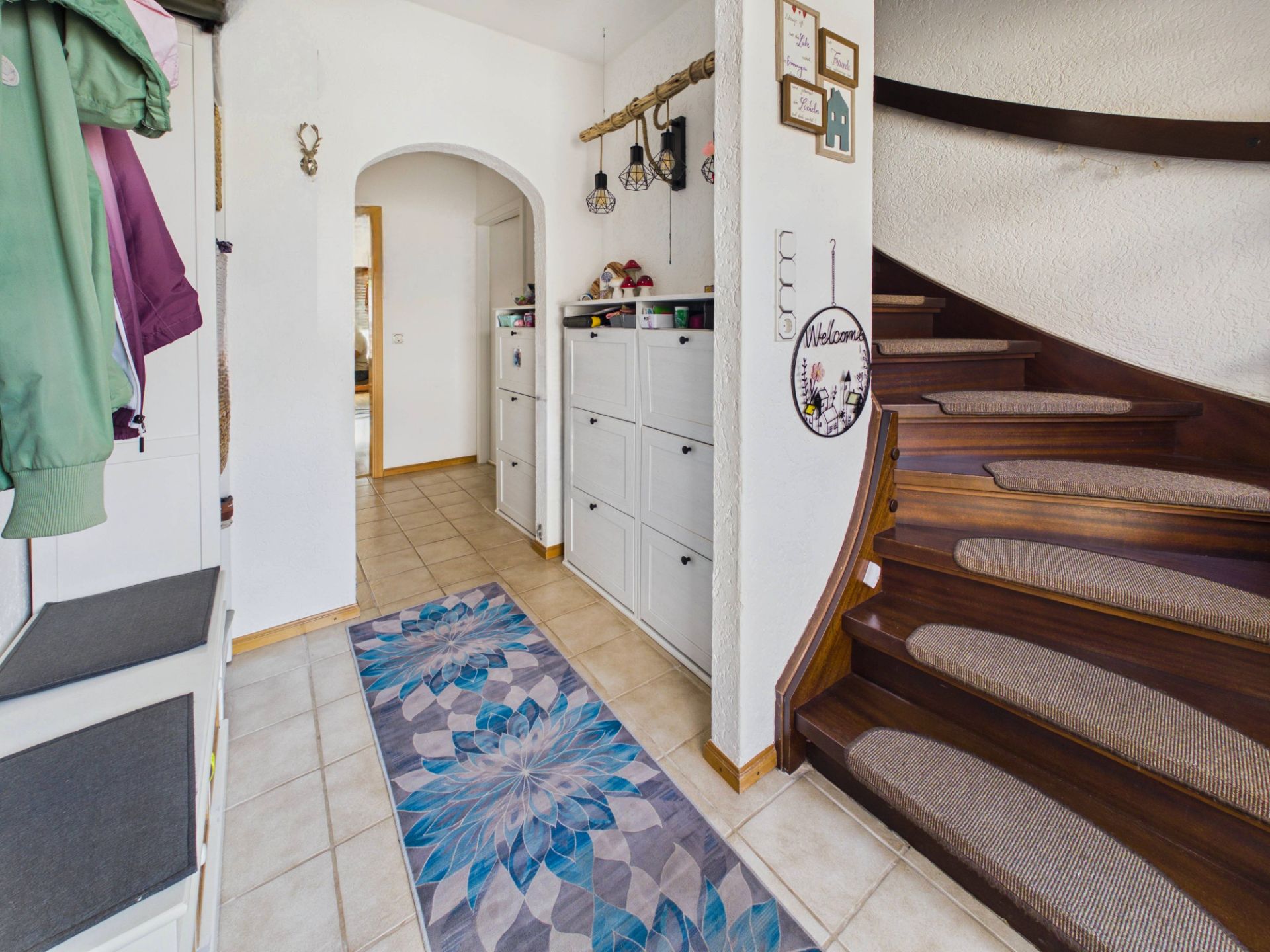 Eingangsbereich mit Flurgarderobe, Teppichläufer und einer Holztreppe mit Teppichstufen.