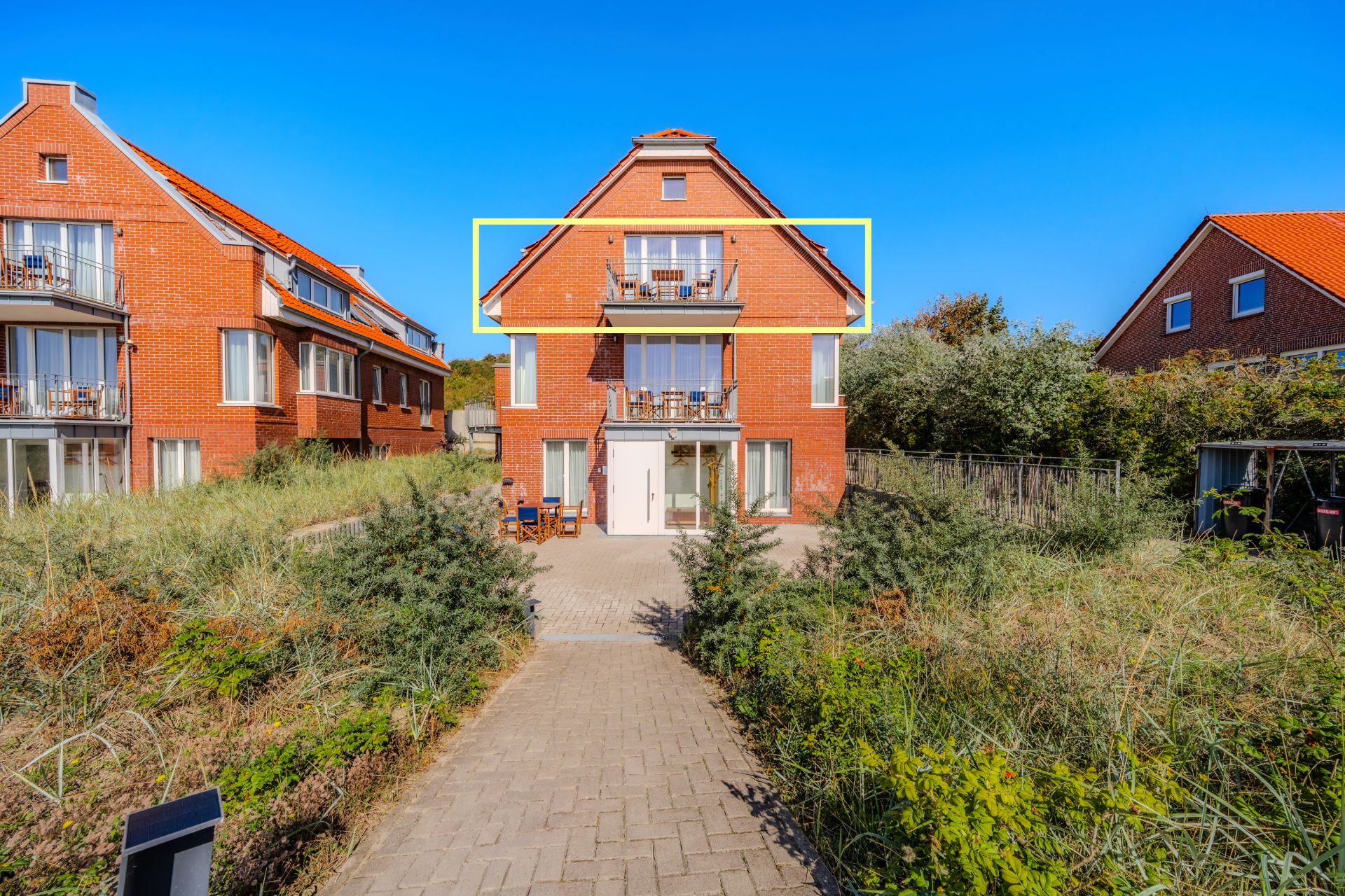 Rotes Backsteinhaus mit zwei Balkonen und Garten, Weg führt zum Eingang.