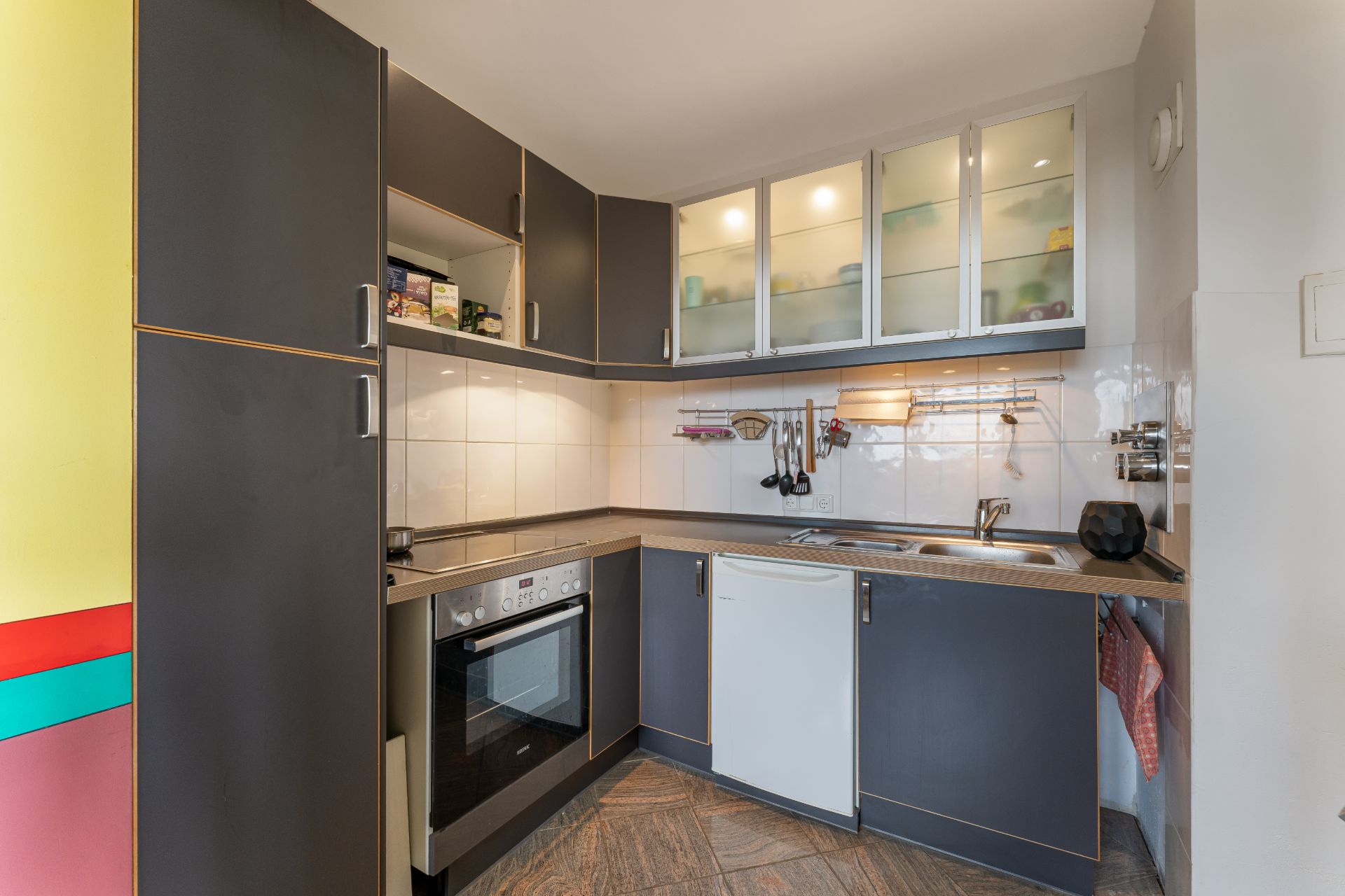 Moderne Einbauküche mit dunklen Schränken, Herd, Kühlschrank und Spüle in einer Ecke.