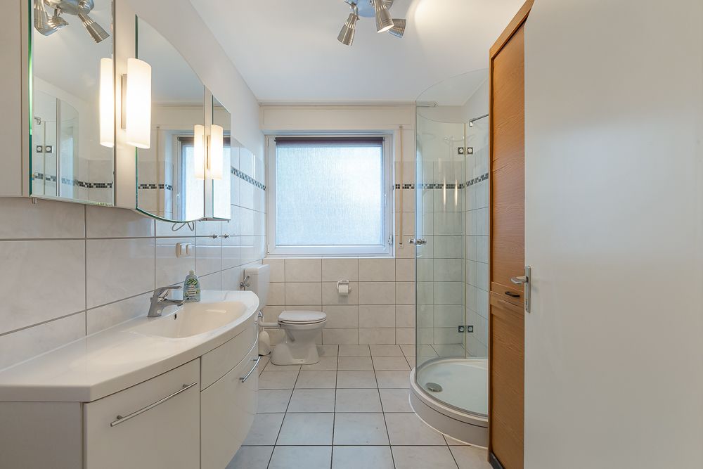 Modernes Badezimmer mit Dusche, Waschbecken, Spiegel, Toilette und einem großen Fenster.