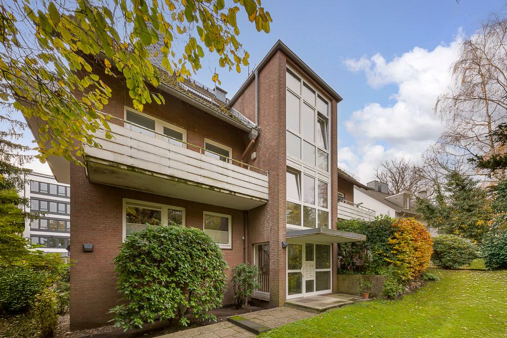 Mehrstöckiges Wohngebäude mit großen Fenstern, Balkon und umgebendem Garten.