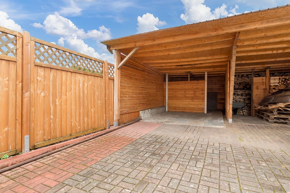 Überdachter Carport aus Holz mit angrenzendem Holzzaun und Holzlagerbereich.
