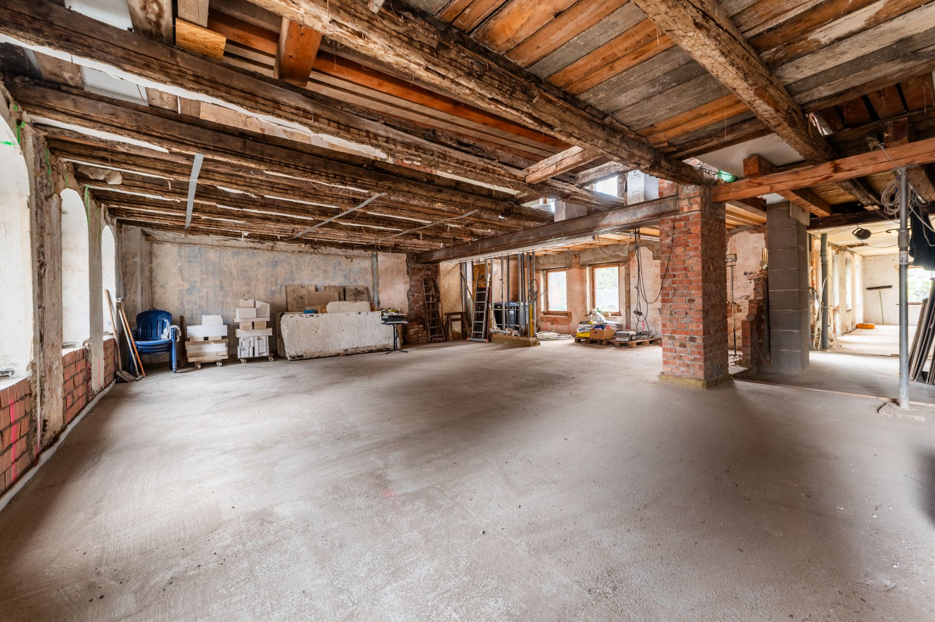 Großer Raum mit freiliegenden Holzbalken, unverputzten Wänden und Baumaterialien.