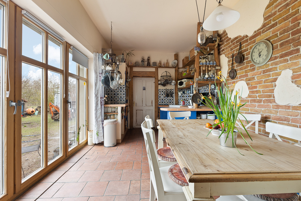 Helle Küche mit Esstisch, Holzmöbeln, Backsteinwand und großen Fenstern zum Garten.