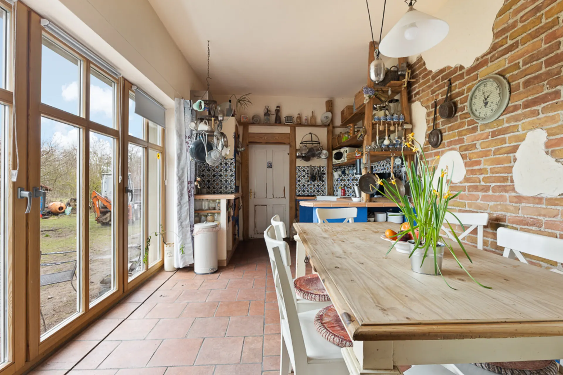 Helle Küche mit Esstisch, Holzmöbeln, Backsteinwand und großen Fenstern zum Garten.