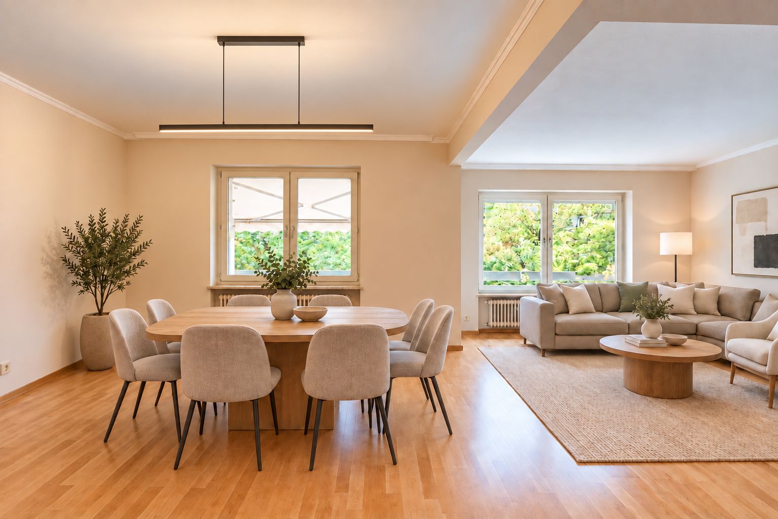 Helles Wohnzimmer mit Essbereich, rundem Holztisch, grauen Stühlen und Sofa, große Fenster mit Blick ins Grüne.