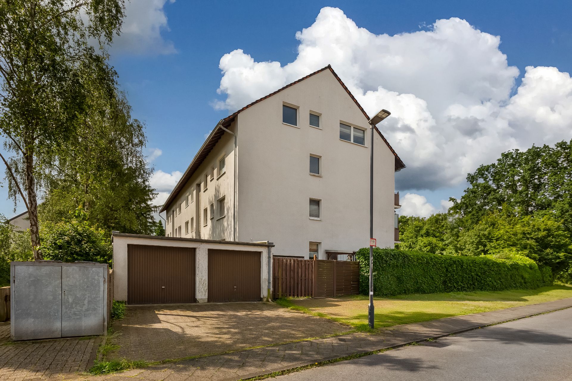 Mehrfamilienhaus mit weißer Fassade, zwei Garagen und grünem Garten im Vordergrund.