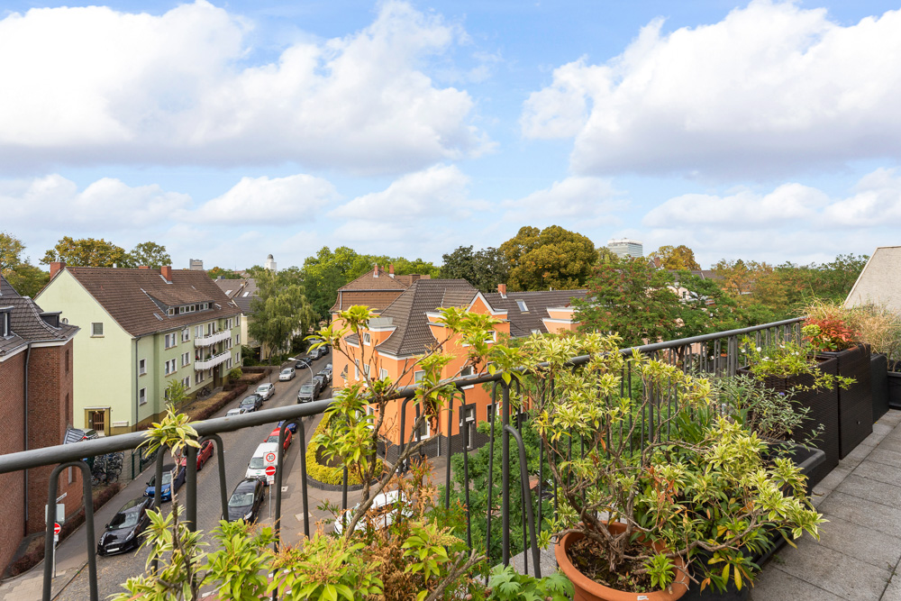 Balkon mit vielen Pflanzen und Blick auf Wohnhäuser und eine ruhige Straße.