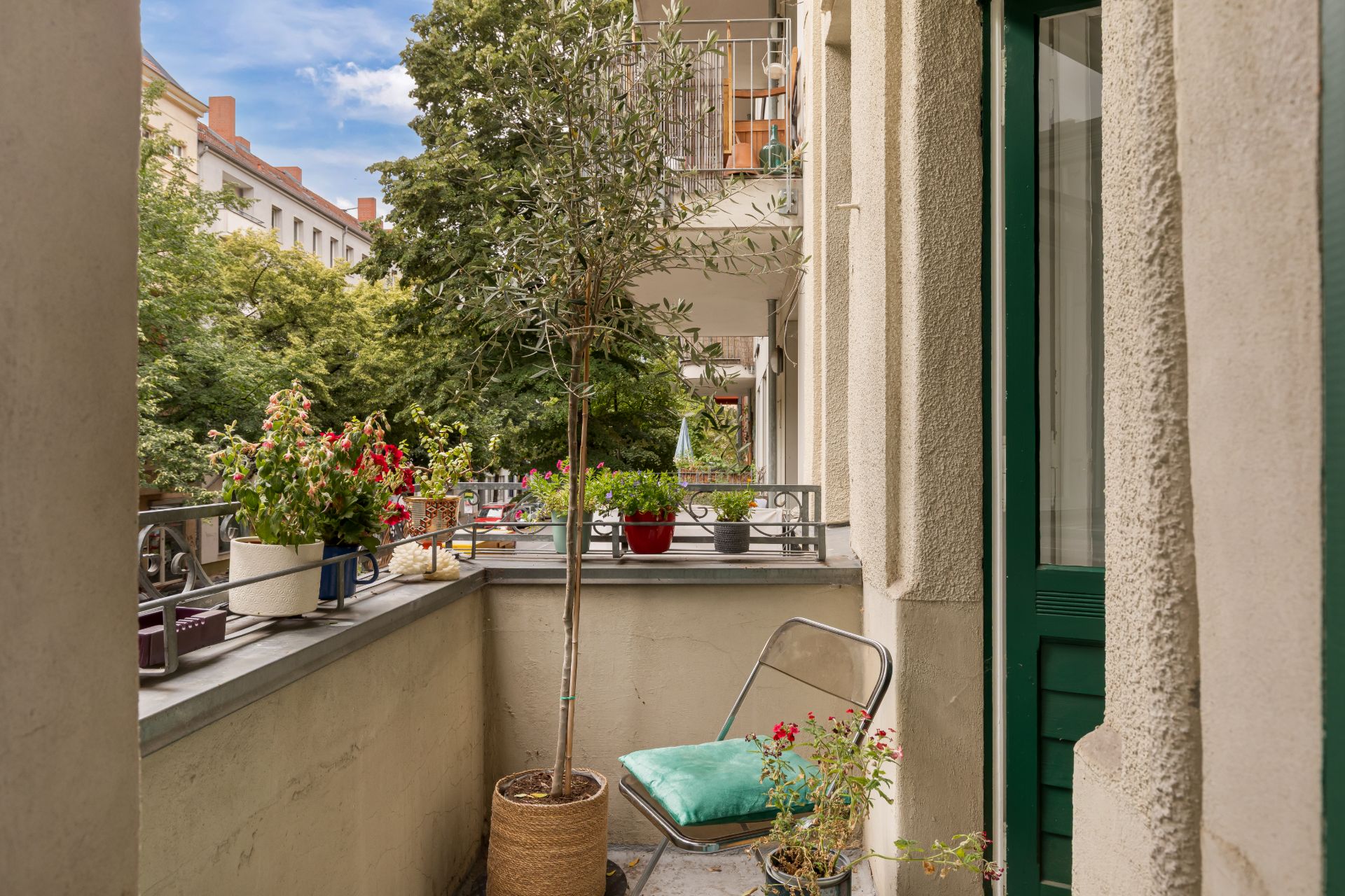 Balkon mit Pflanzen, Stuhl und Topfbaum, Blick auf grüne Bäume und Nachbarbalkone.