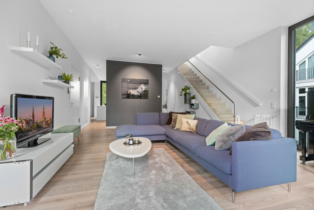 Modernes Wohnzimmer mit großer blauer Eckcouch, Fernseher, Couchtisch und Treppe im Hintergrund.