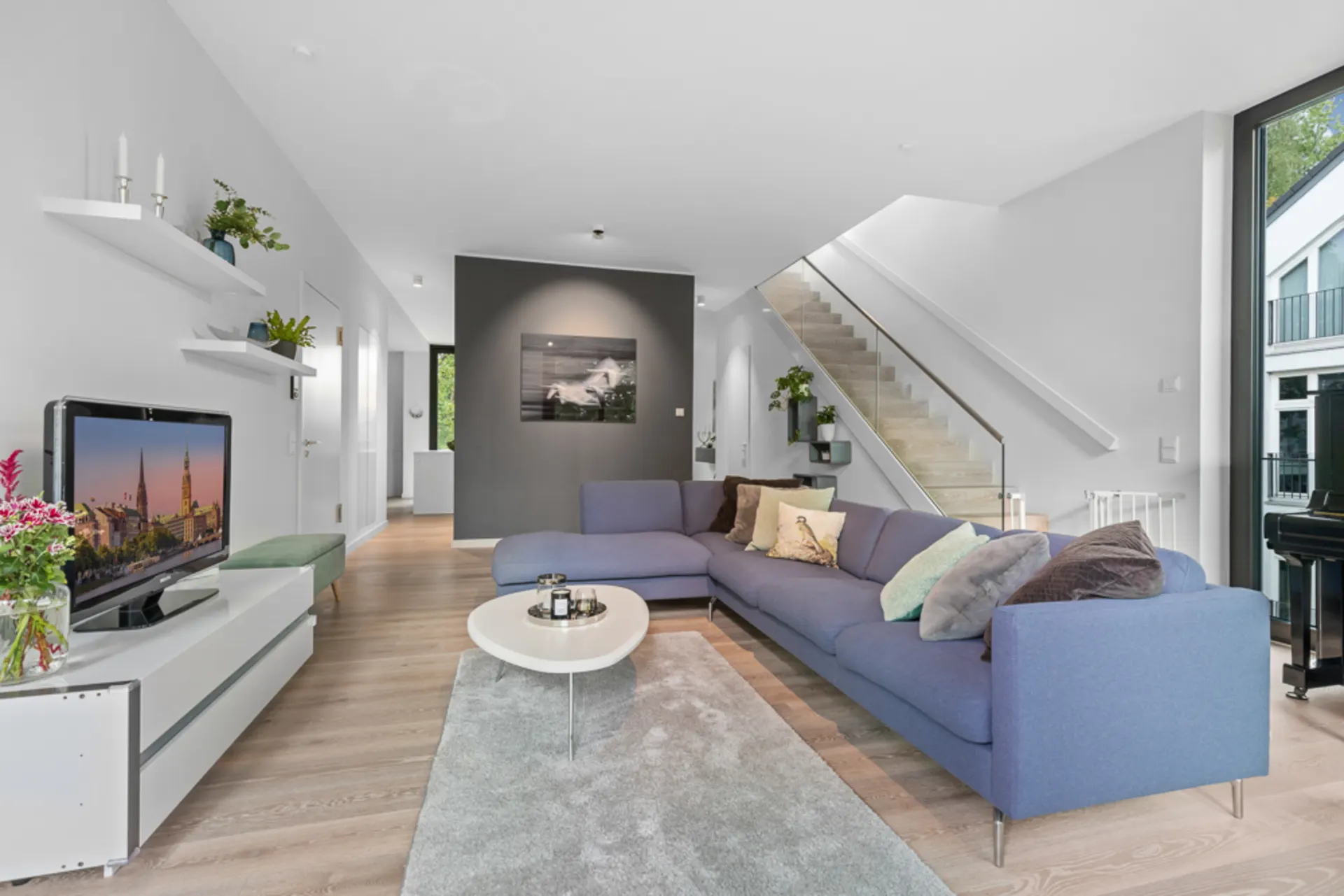 Modernes Wohnzimmer mit großer blauer Eckcouch, Fernseher, Couchtisch und Treppe im Hintergrund.