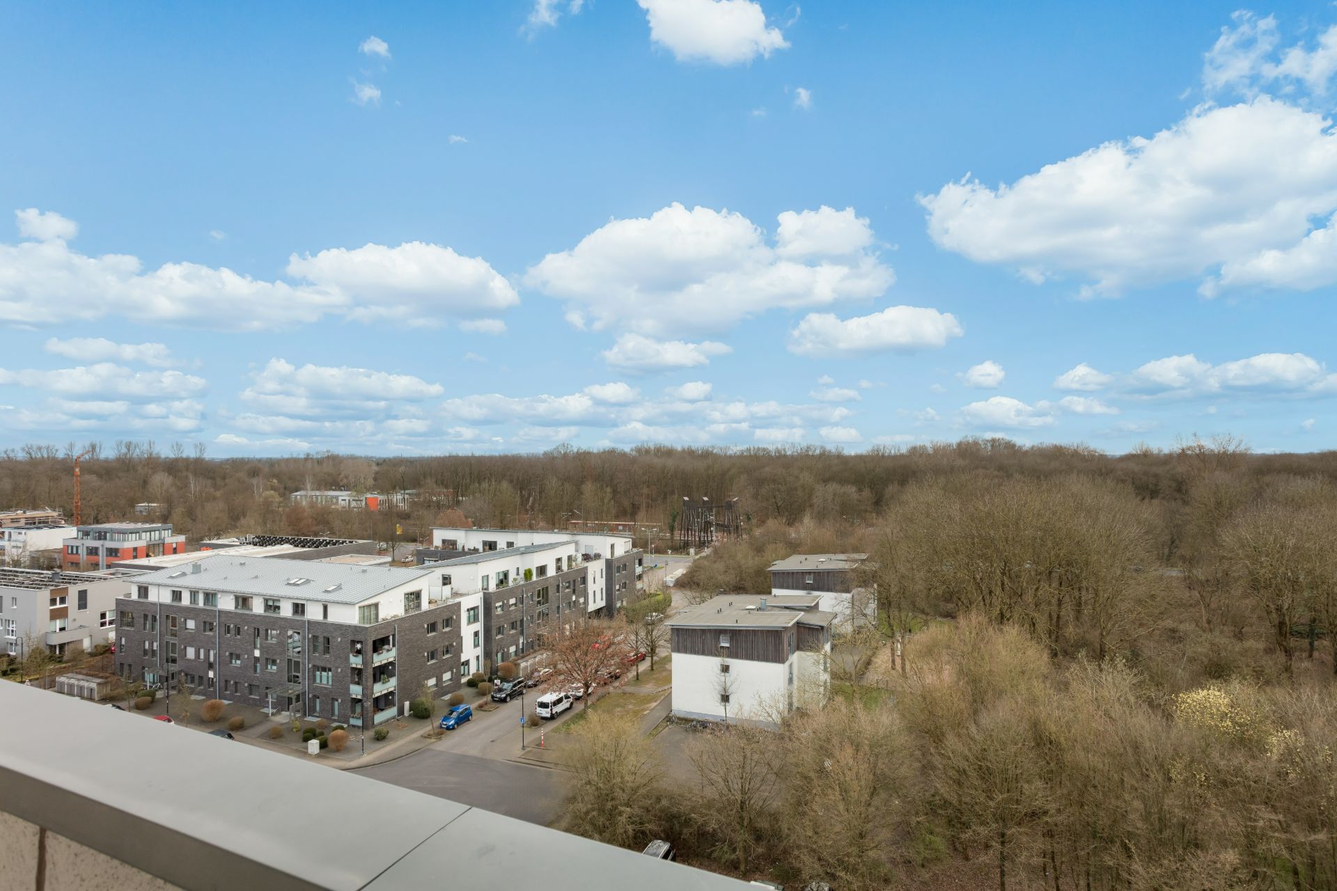 Blick auf Wohngebäude und Bäume unter blauem Himmel mit weißen Wolken.