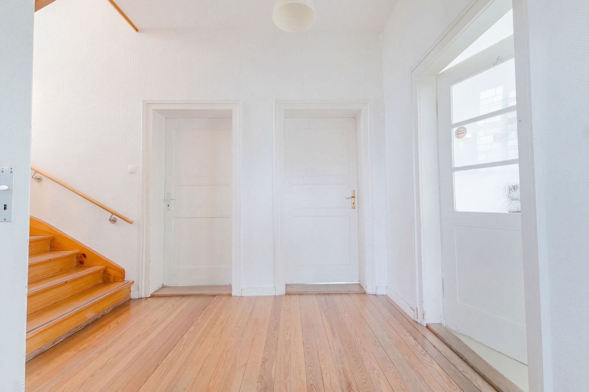 Heller Flur mit Holzboden, zwei weißen Türen, Treppe und Glastür.