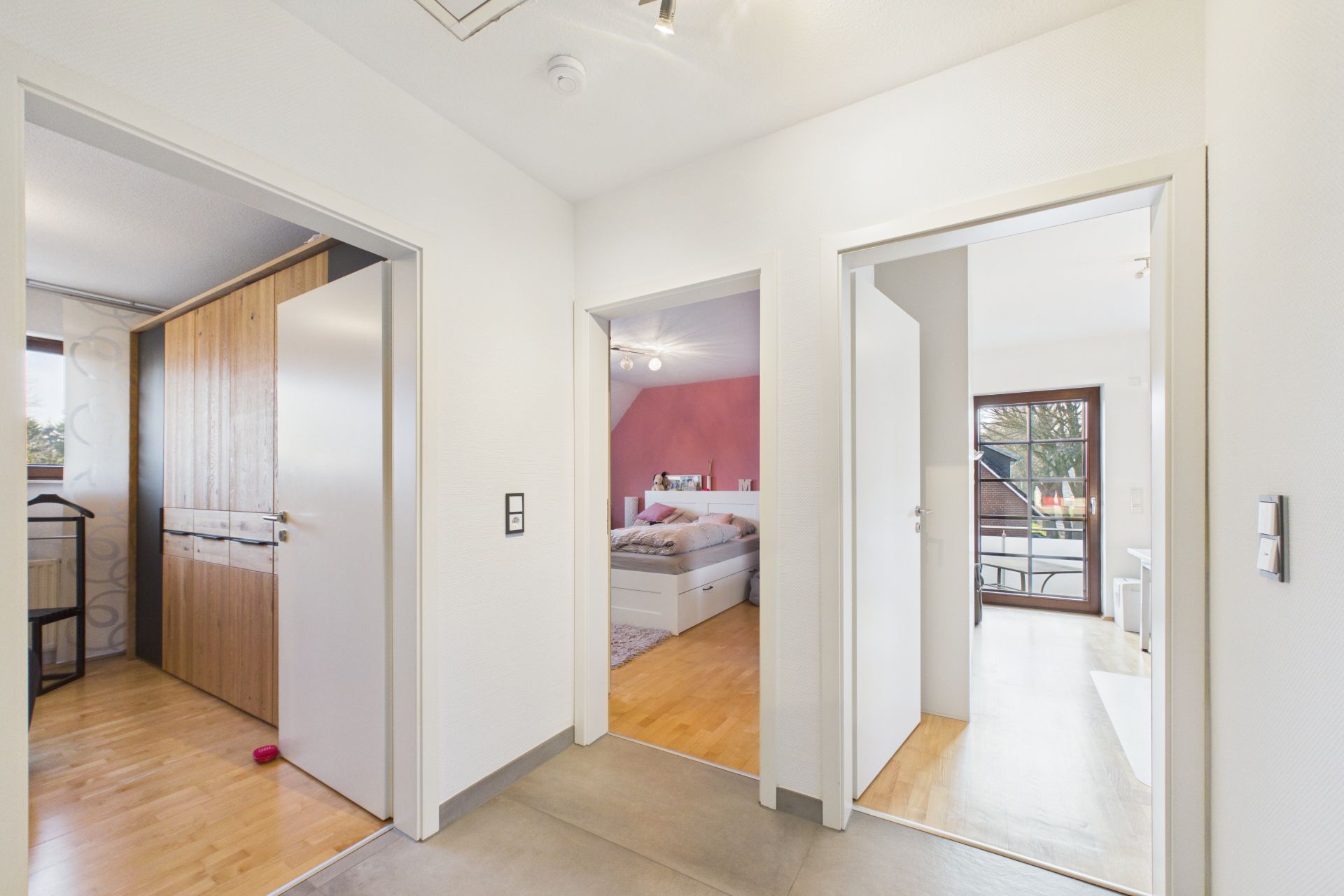 Heller Flur mit drei offenen Türen zu Schlafzimmern und einem Schrank.