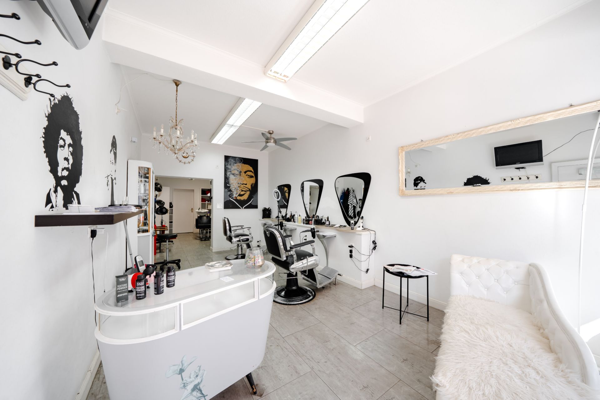 Heller Friseursalon mit Spiegeln, Stühlen, Wandbildern und Wartebereich mit Sofa.