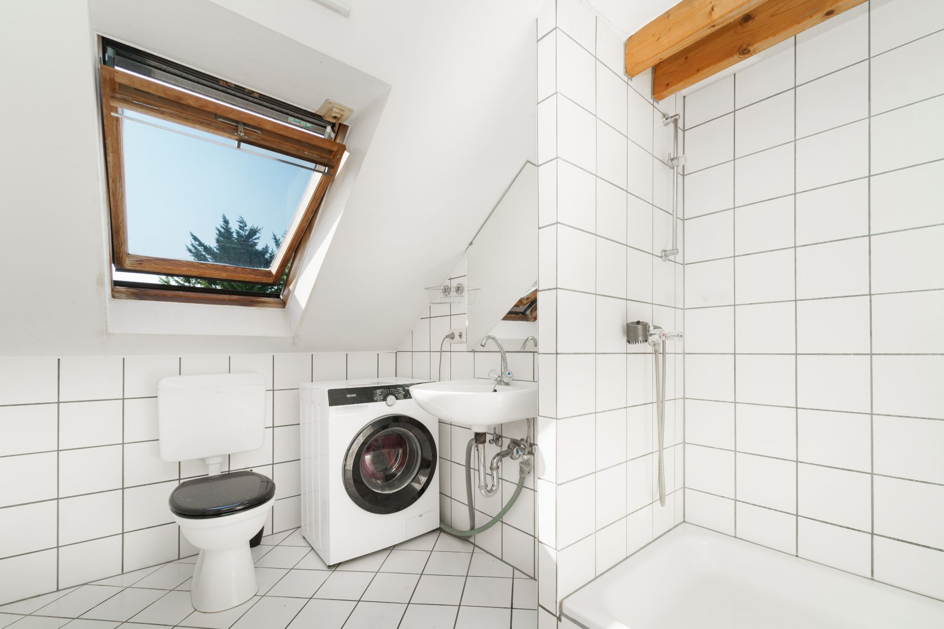 Helles Bad mit Dachfenster, Toilette, Waschmaschine, Waschbecken und Dusche mit weißen Fliesen.