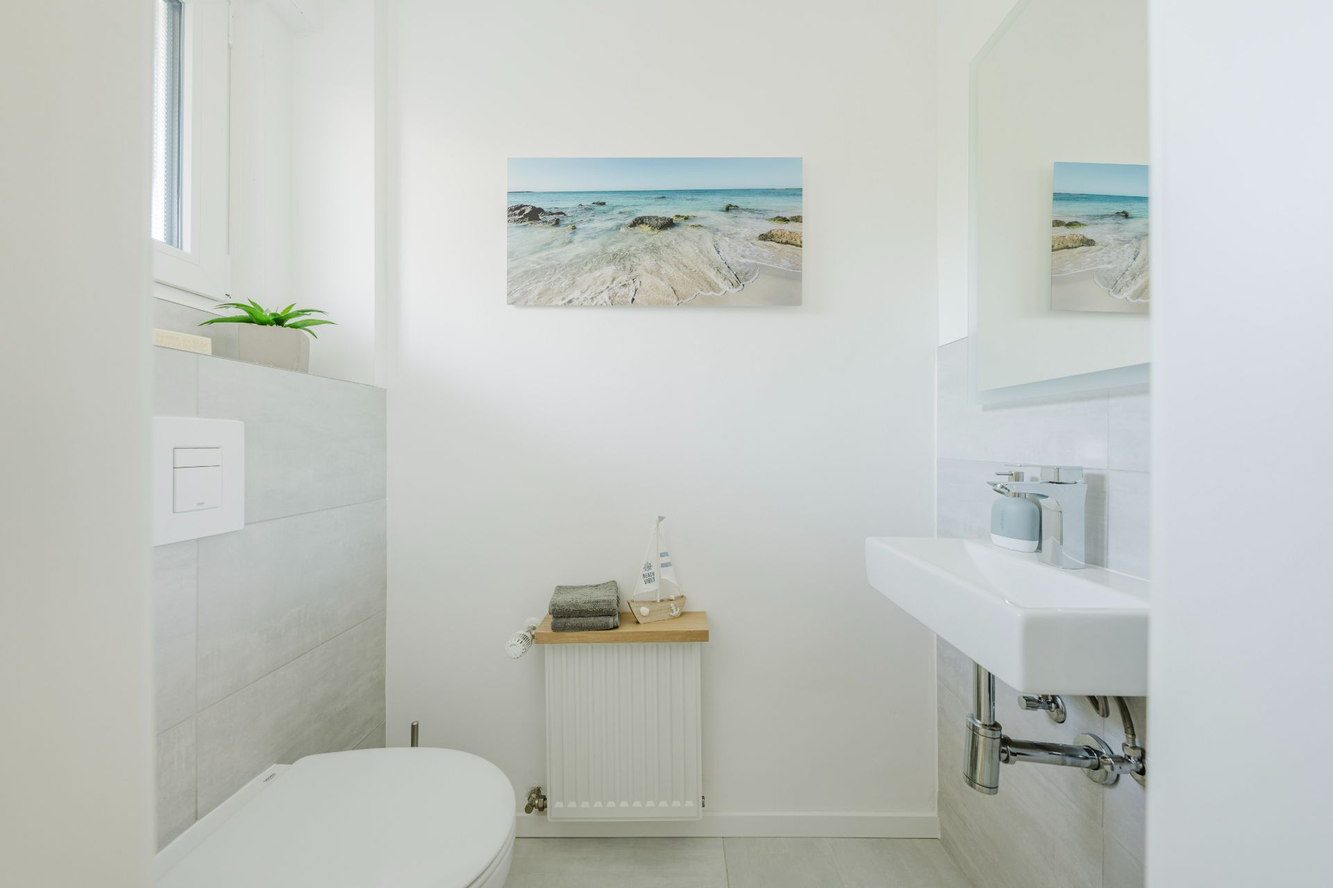 Helles Badezimmer mit Toilette, Waschbecken, Bild an der Wand und kleinem Fenster.