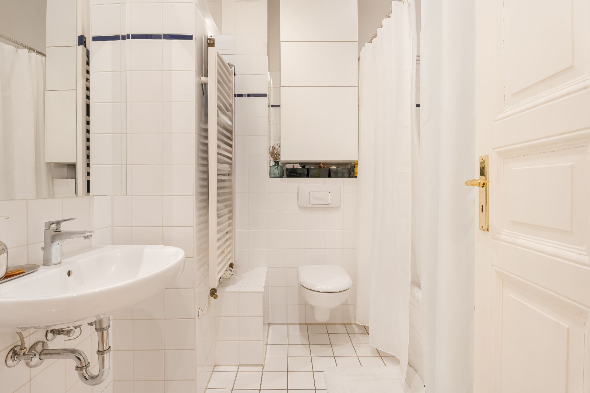 Helles Badezimmer mit Waschbecken, Toilette, Heizkörper und Dusche mit Duschvorhang.