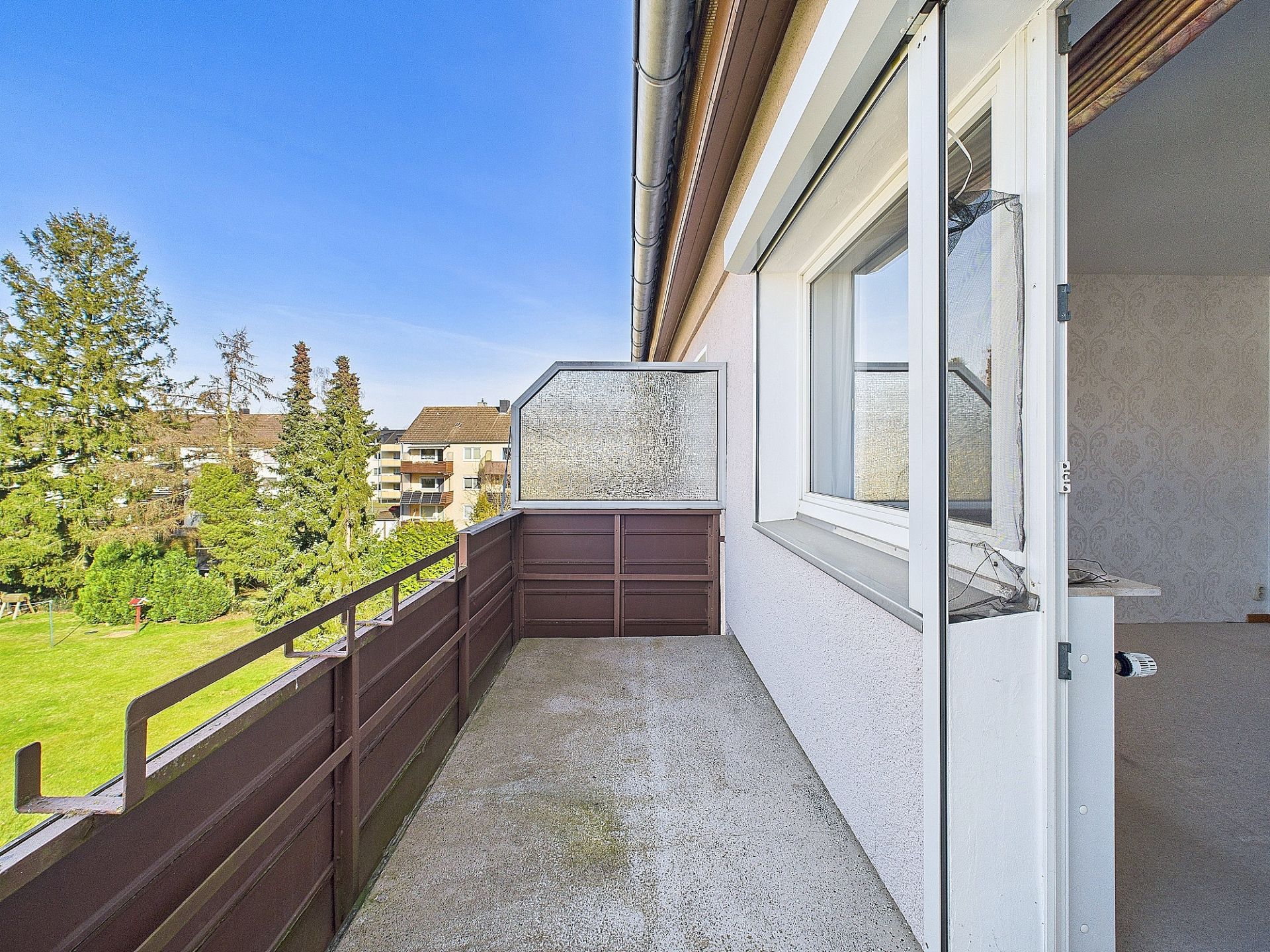 Balkon mit braunem Geländer und Blick auf grüne Wiese und Bäume.