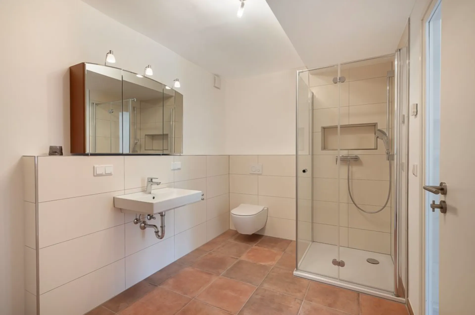 Modernes Badezimmer mit Dusche, Wandspiegel, Waschbecken und wandhängender Toilette.