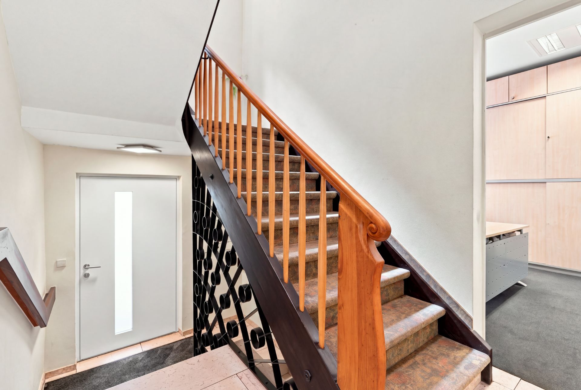 Treppenhaus mit Holzgeländer und Zugang zu einem Raum mit hellen Einbauschränken.