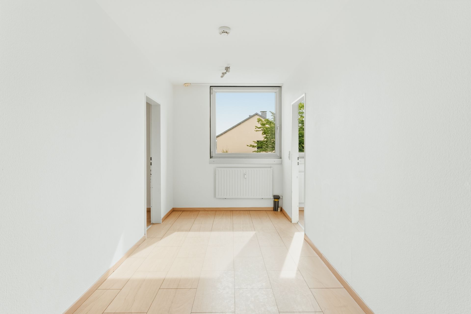 Heller Flur mit Fenster, zwei Türen, weiß gestrichenen Wänden und hellem Holzboden.
