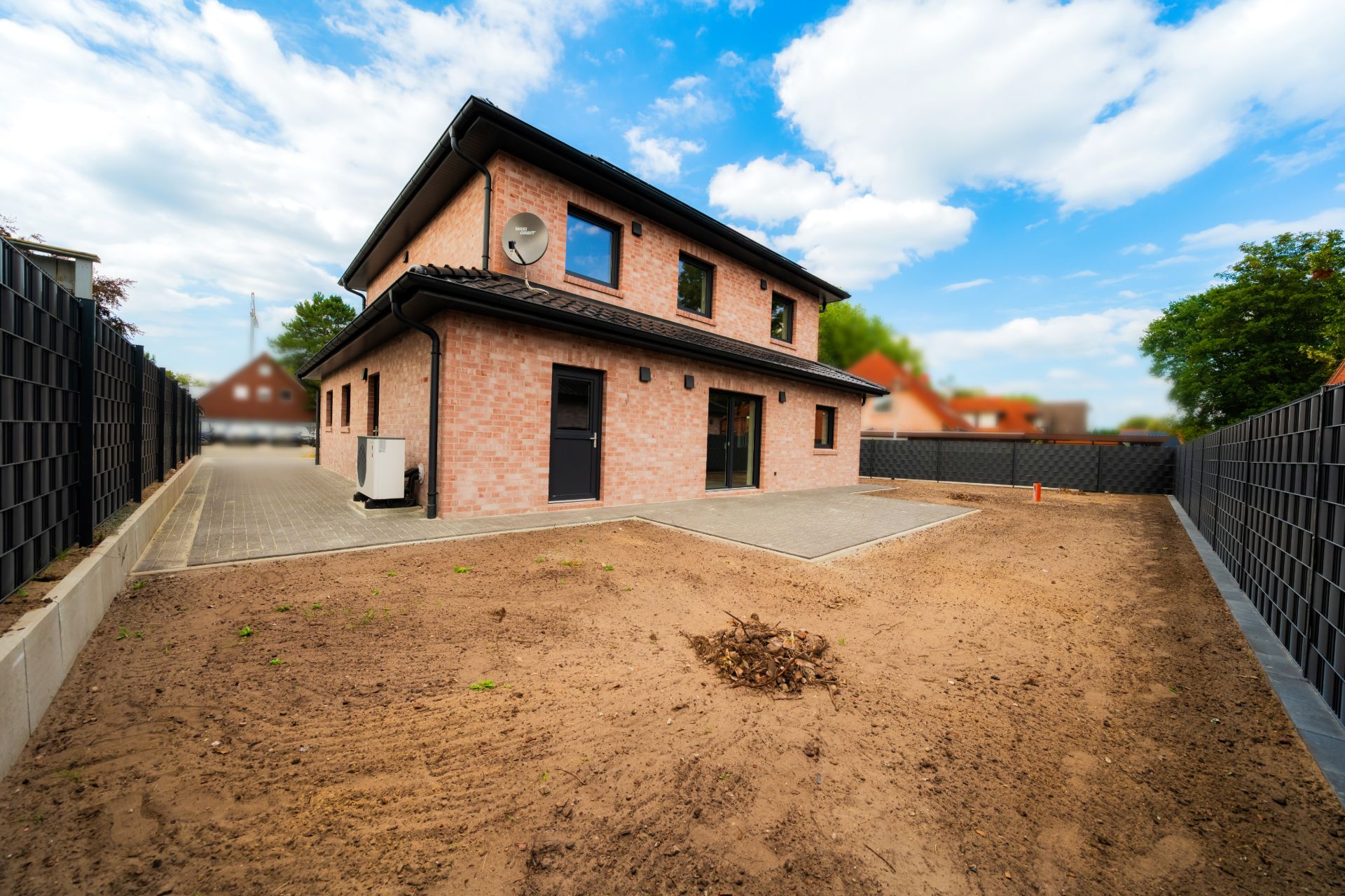 Zweistöckiges Backsteinhaus mit Gartenfläche und gepflastertem Weg, umgeben von einem Zaun.