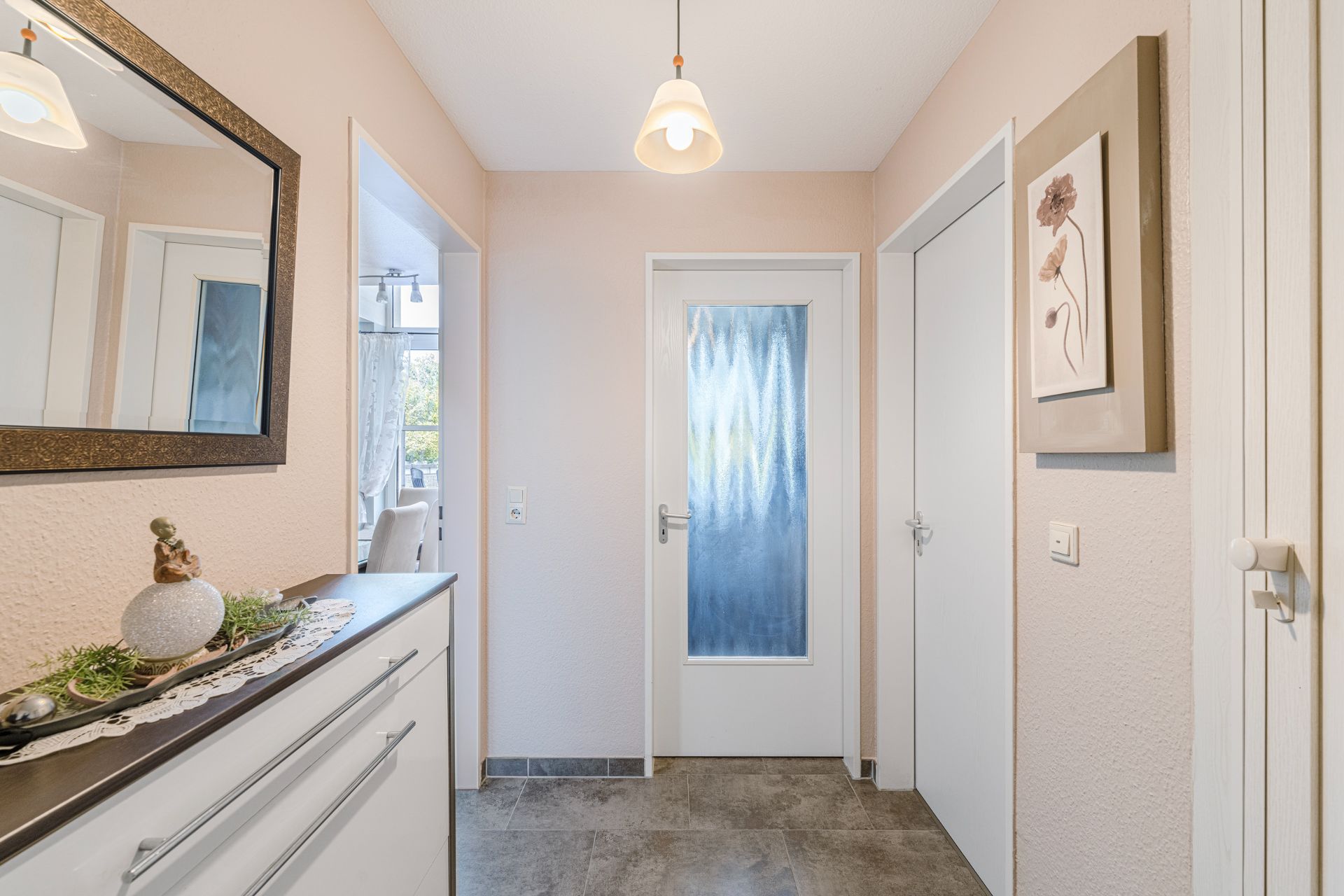Heller Flur mit Spiegel, Kommode, Hängeleuchte und Türen, Bild mit Blumen an der Wand.