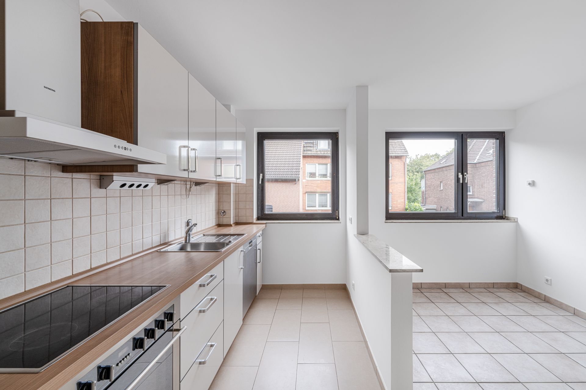 Moderne Einbauküche mit Herd, Spüle und weißen Schränken, zwei große Fenster im Raum.