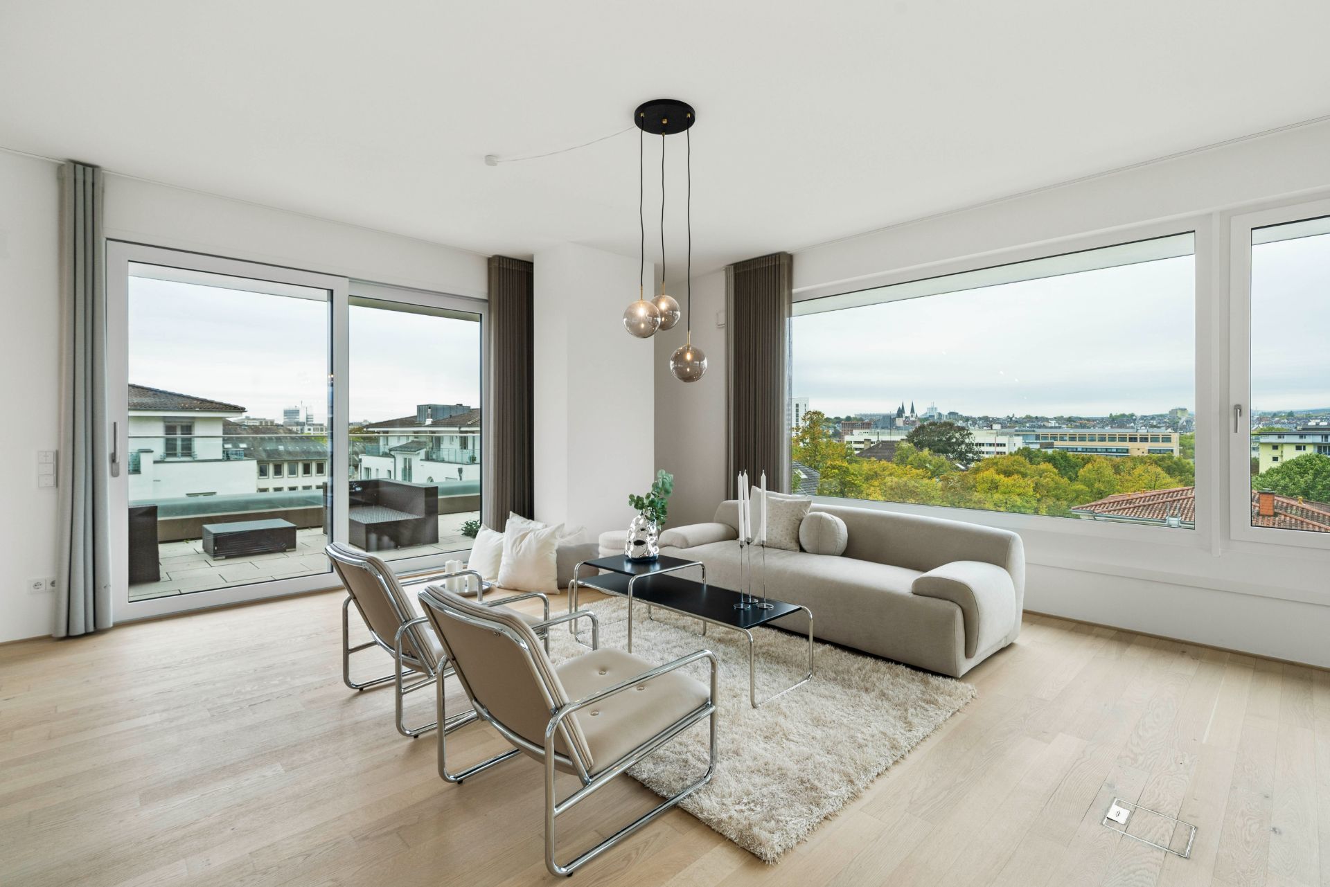 Modernes Wohnzimmer mit großen Fenstern, Sofa, Sesseln und Blick auf Stadt und Terrasse.