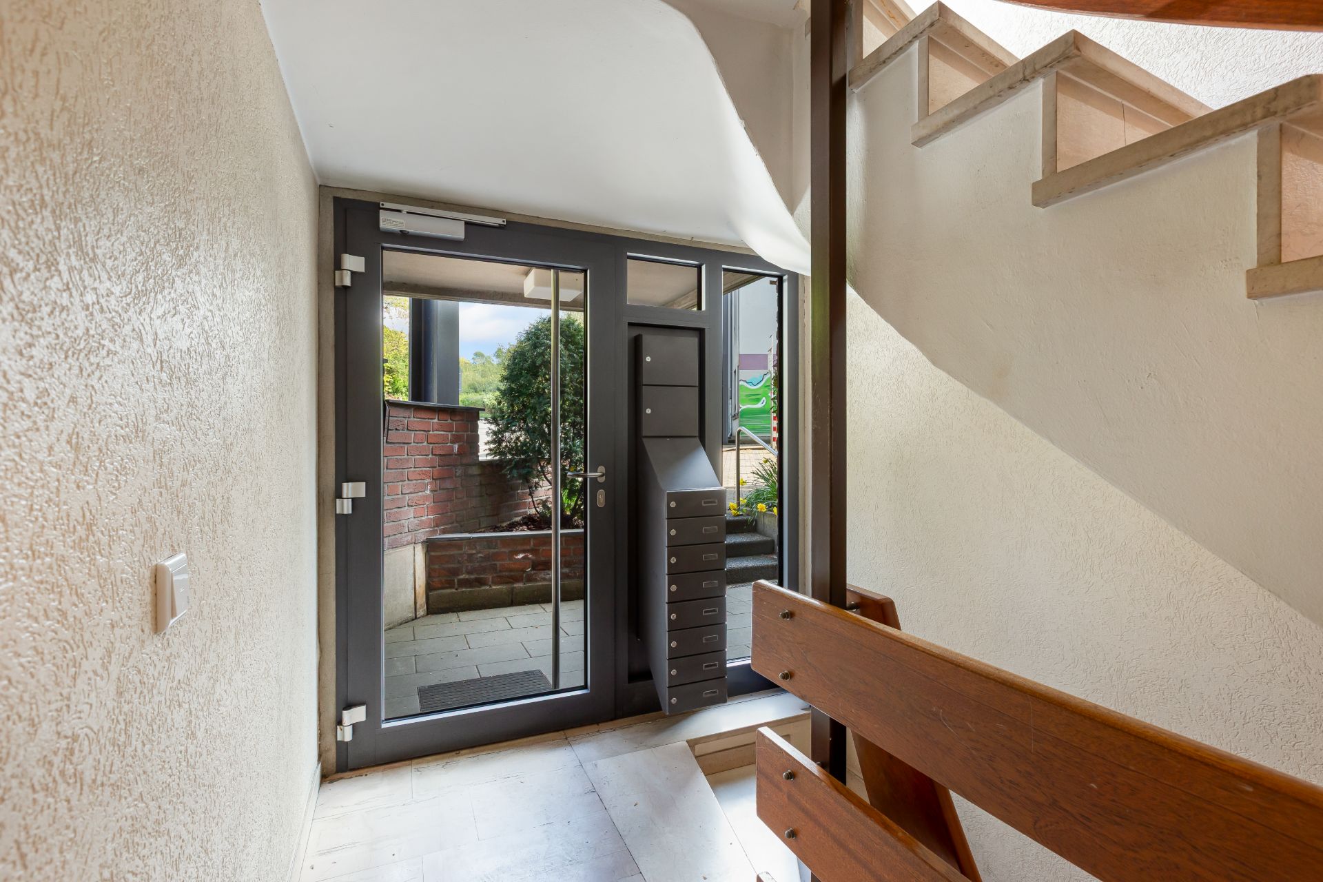 Hauseingang mit Glastür, Briefkästen und Treppe nach oben, Blick nach draußen.