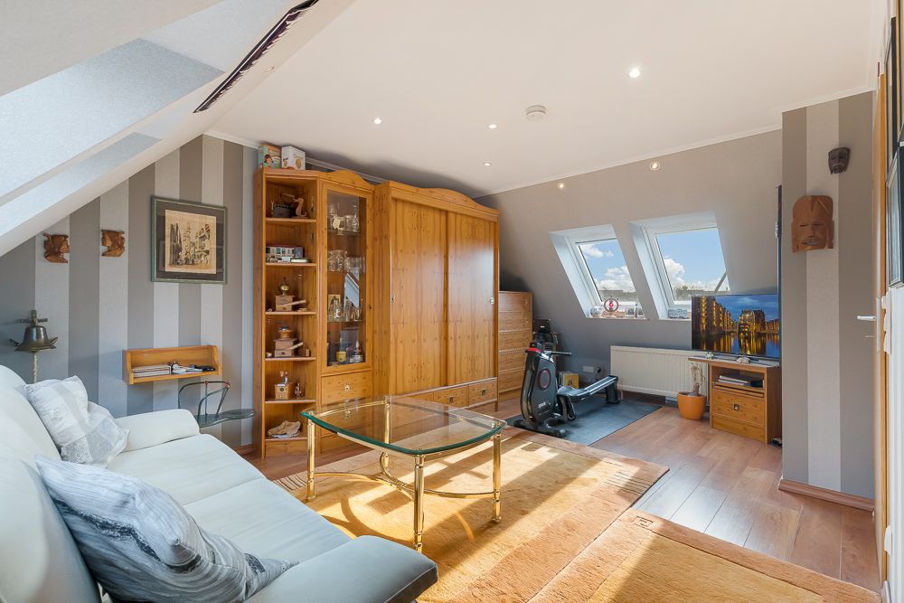 Helles Wohnzimmer mit Sofa, Glastisch, Holzschrank und zwei Dachfenstern.