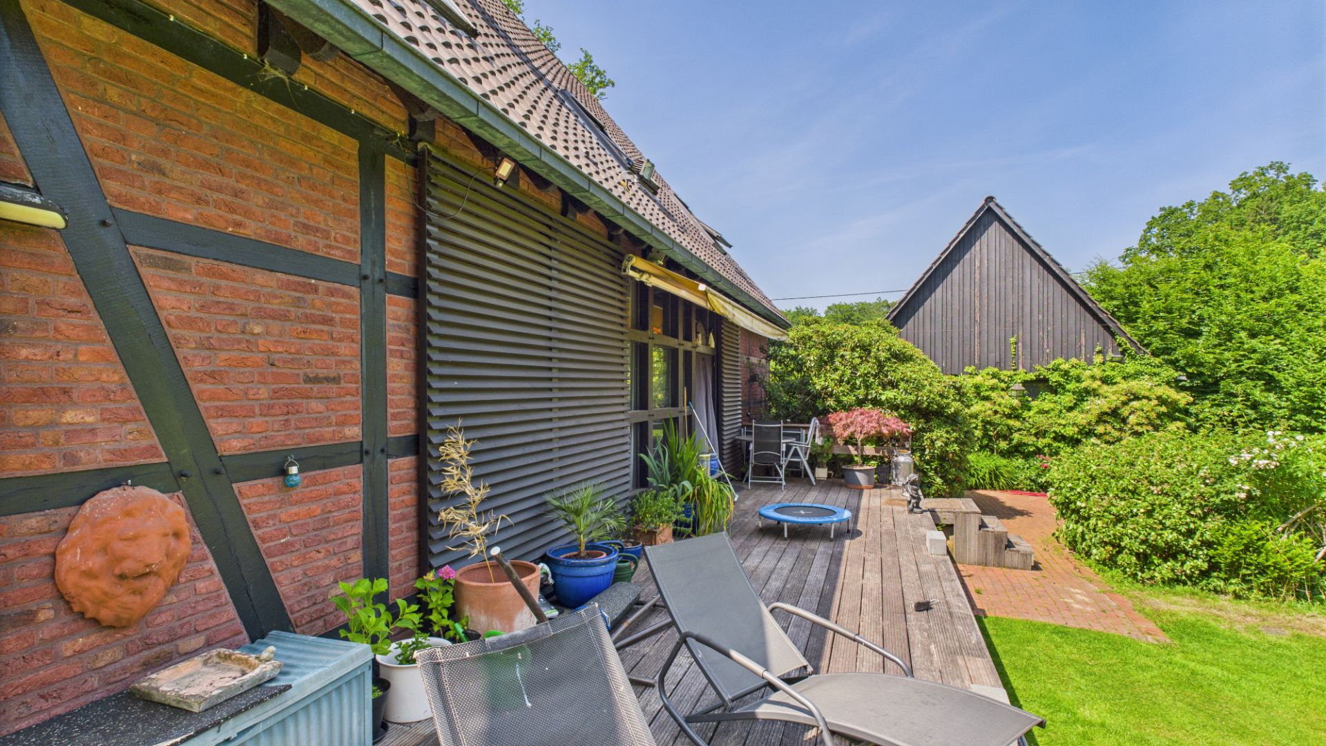Holzterrasse mit Liegestühlen, Pflanzen und Blick auf grünen Garten an einem Wohnhaus.