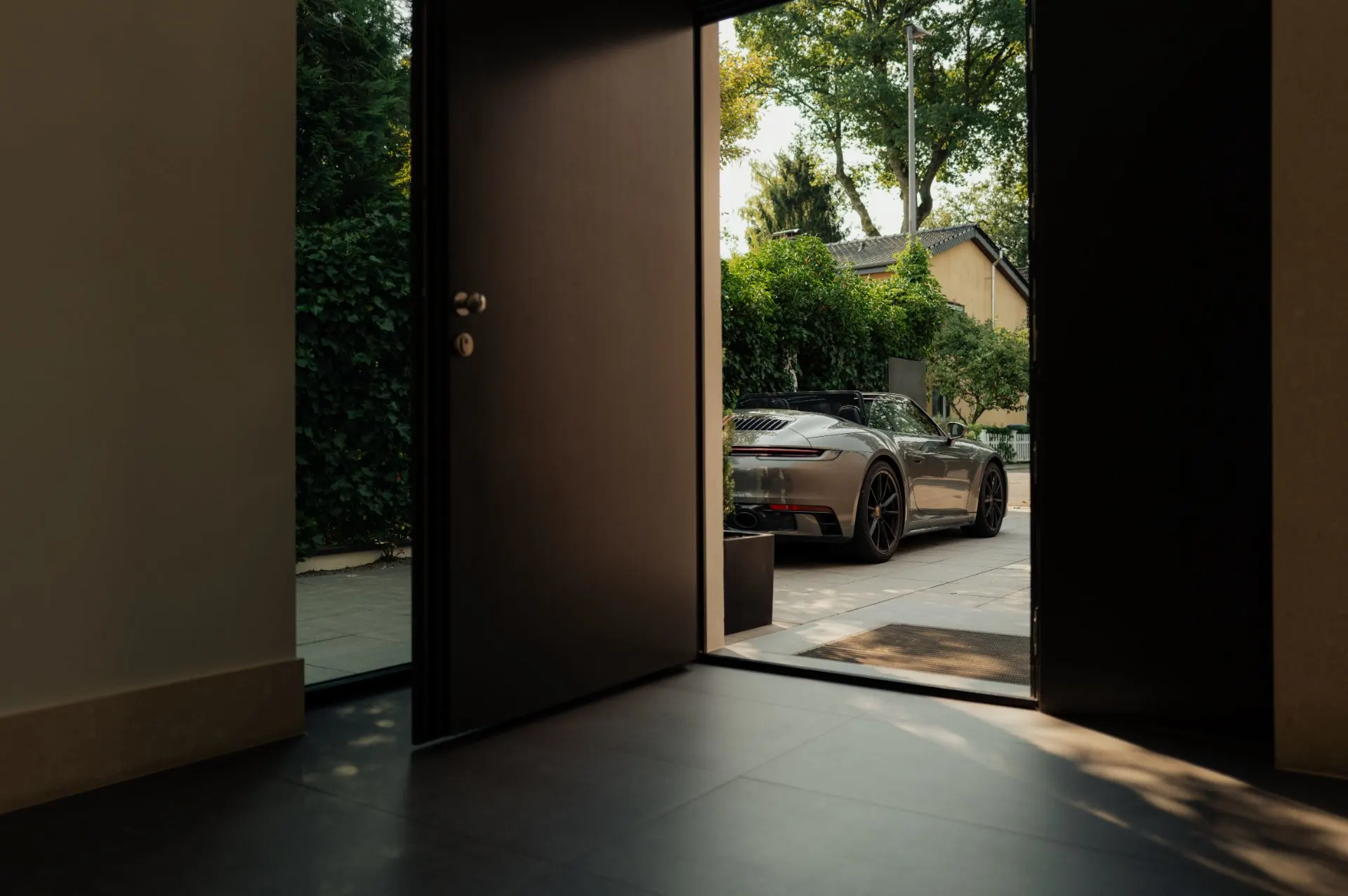 Offene Haustür mit Blick auf ein geparktes Auto in der Einfahrt und Bäume im Hintergrund.