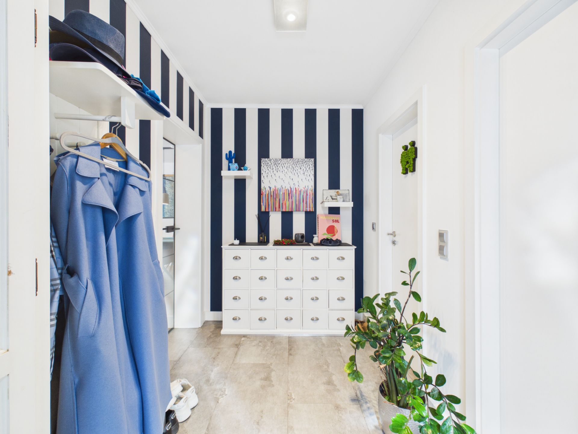 Heller Flur mit weiß-blau gestreifter Wand, Kommode, Garderobe und Zimmerpflanze.