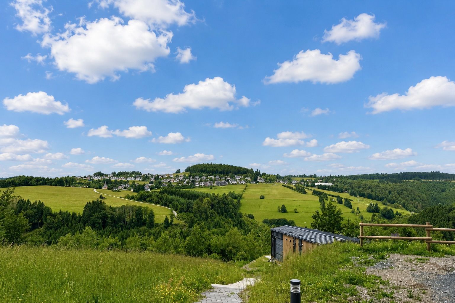 Blick auf eine grüne Hügellandschaft mit Wiesen, Bäumen und einem kleinen Schuppen im Vordergrund.