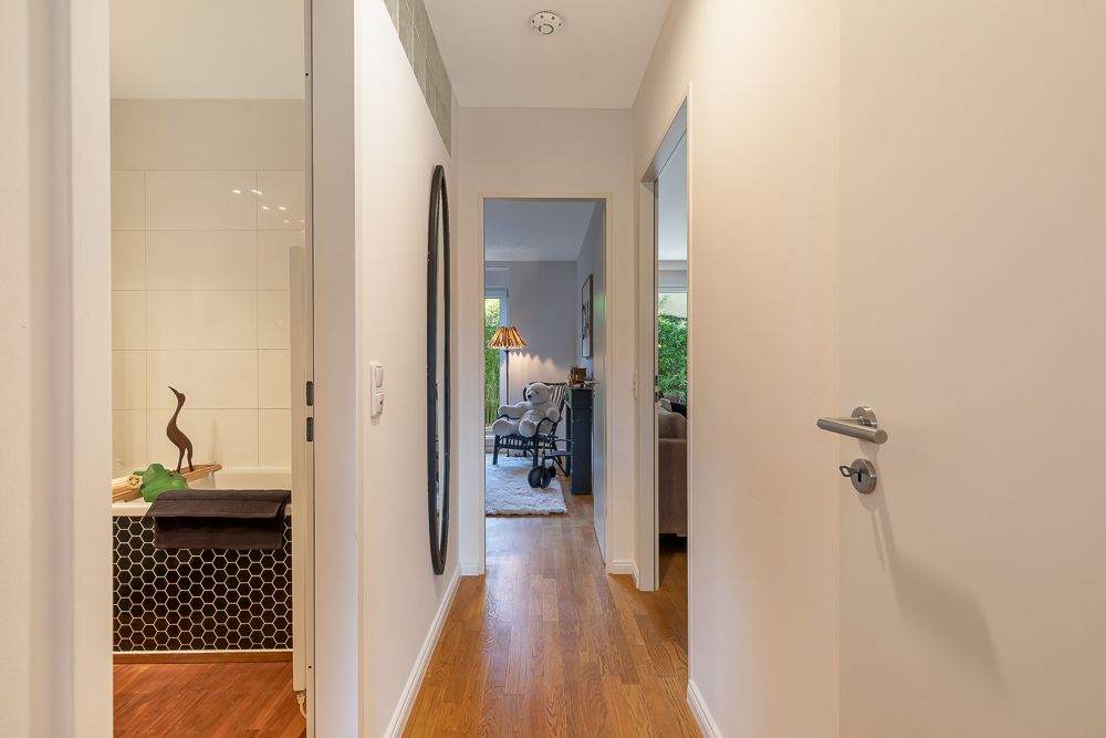 Heller Flur mit Holzboden, links ein Badezimmer, geradeaus ein Wohnzimmer mit Sessel.