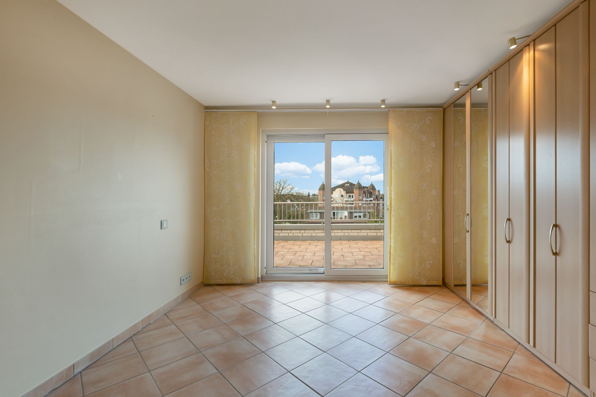 Helles Zimmer mit Fliesenboden, Einbauschrank und großer Glastür zur Terrasse.