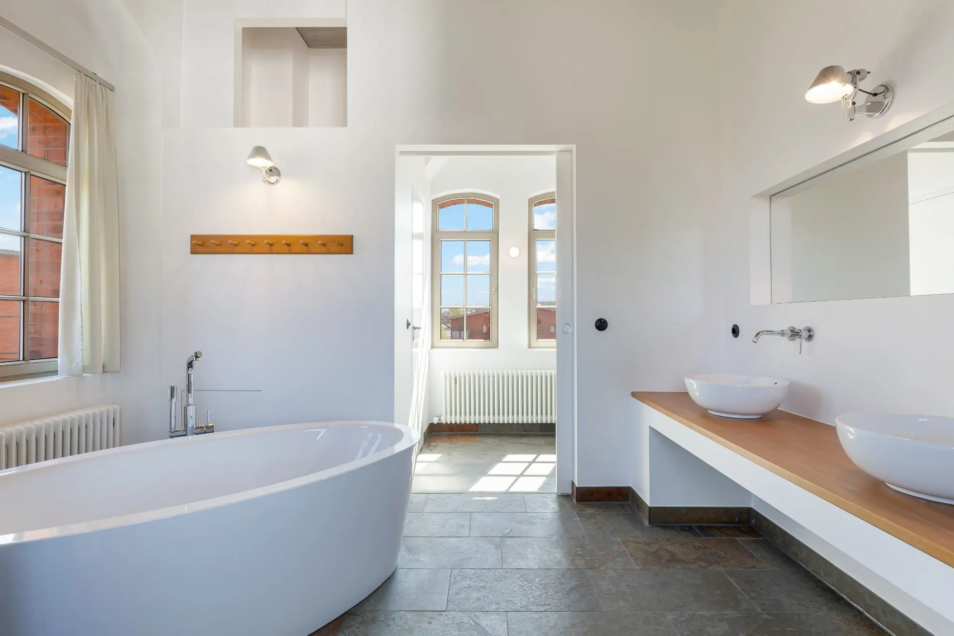 Modernes Badezimmer mit freistehender Badewanne und zwei Waschbecken auf einer Holzplatte.