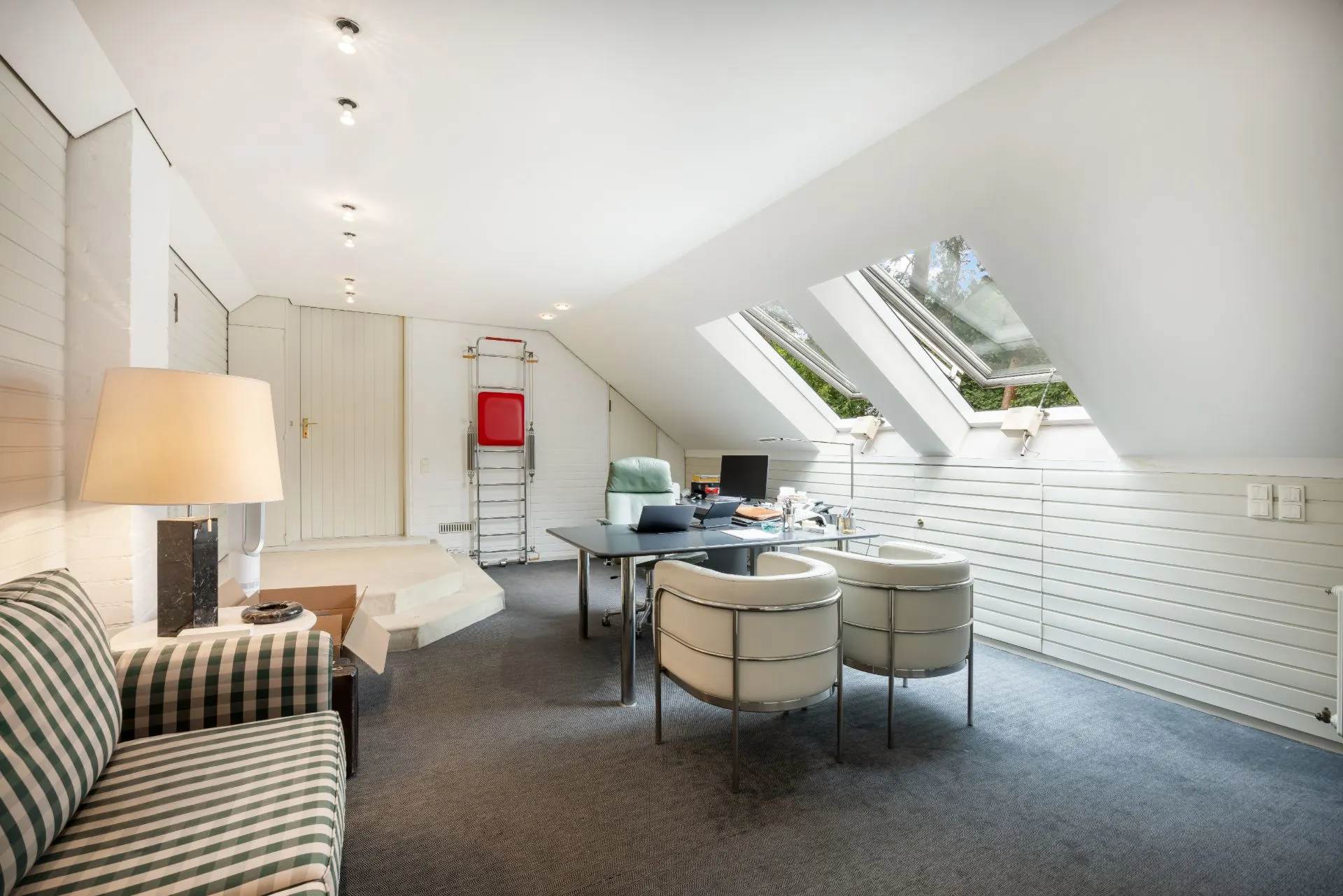 Helles Arbeitszimmer mit Schreibtisch, Stühlen, Sofa und Dachfenstern in einem Dachgeschoss.
