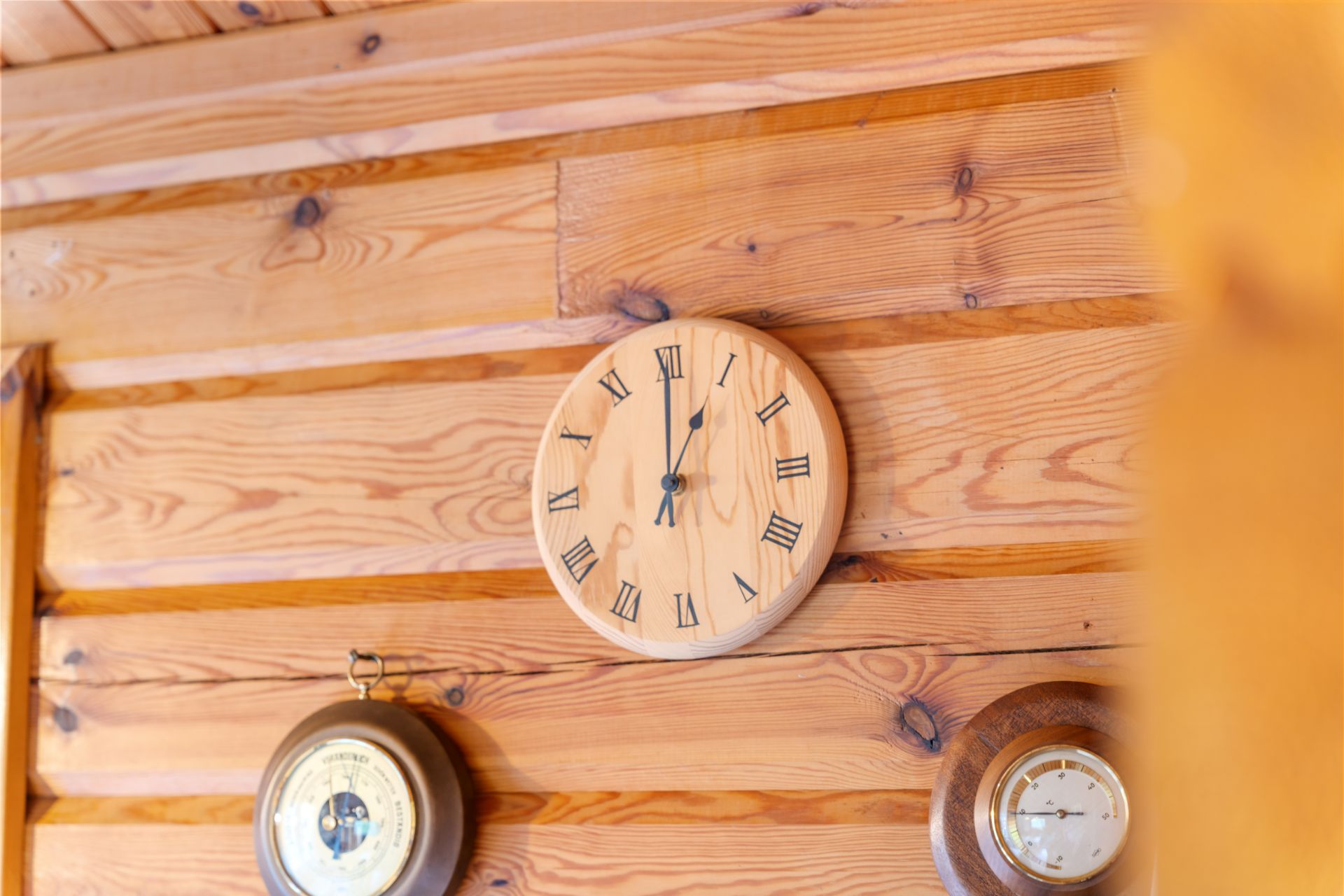 Holzwanduhr mit römischen Ziffern hängt an einer hellen Holzvertäfelung.